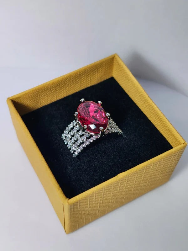 Elegant silver-tone statement ring featuring a large pink oval crystal centerpiece with sparkling clear stones, displayed in a gold gift box with a black velvet interior.
