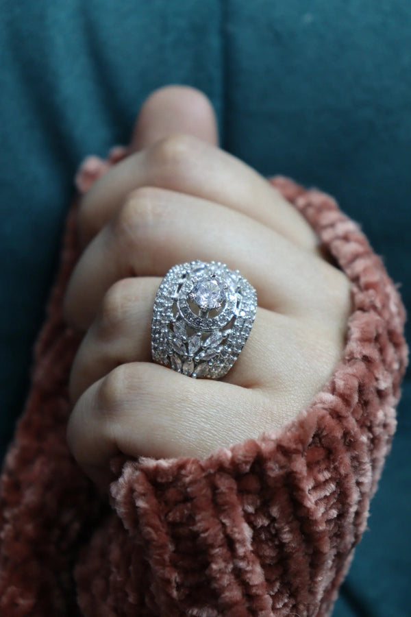 Close-up of a hand wearing an elegant silver-toned statement ring featuring a large round crystal center and intricate sparkling embellishments.