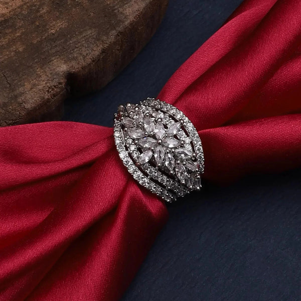 Elegant silver-toned floral statement ring adorned with sparkling clear stones, placed on luxurious red satin fabric against a dark background, showcasing an intricate and glamorous jewellery design.